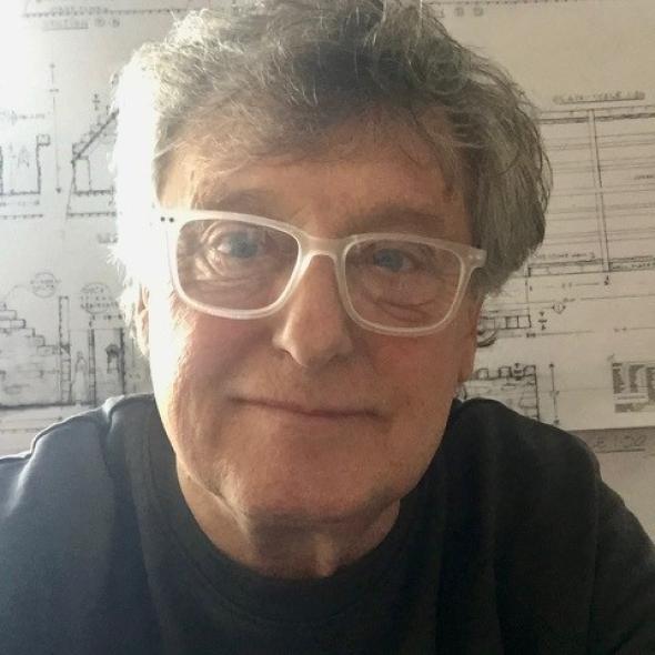 Image of man with grey hair and glasses looks towards camera